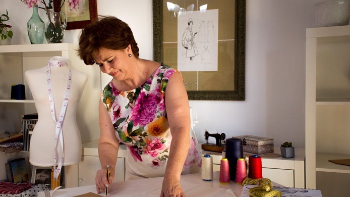 Mari Carmen trazando un patrón, con un maniquí y una máquina de coser antigua al fondo